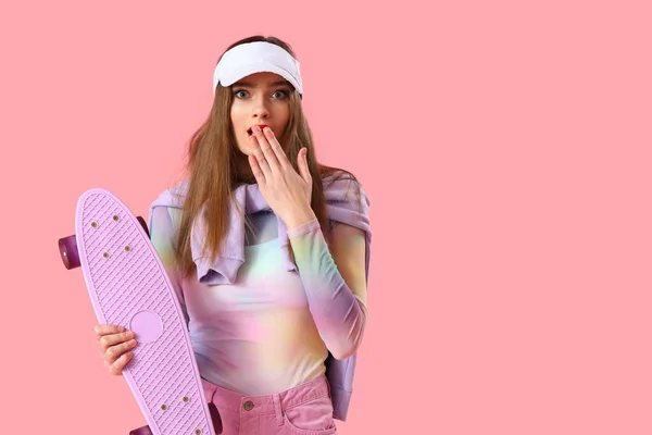 Shocked young woman with skateboard on pink background