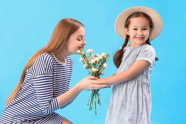可爱的小女孩用蓝色背景的花朵问候她的母亲 — 图库照片