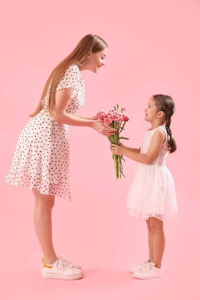 可爱的小女孩用粉色背景的花朵问候她的母亲 — 图库照片