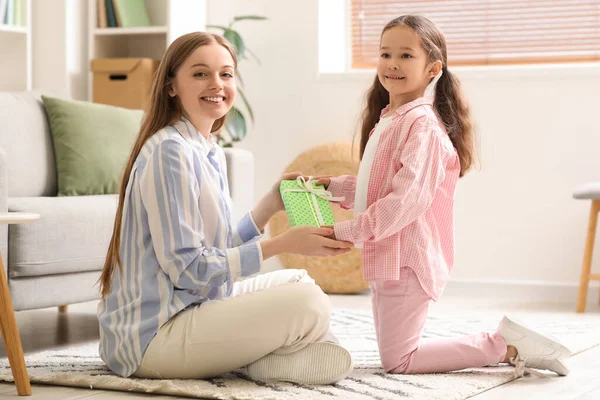 stock image Cute little girl greeting her mother with gift at home