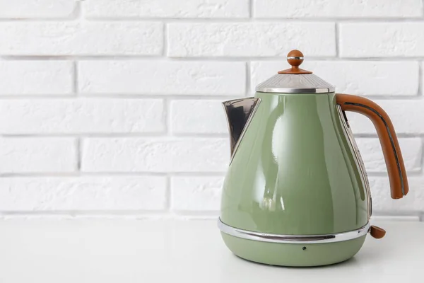 stock image Electric kettle on table near white brick wall