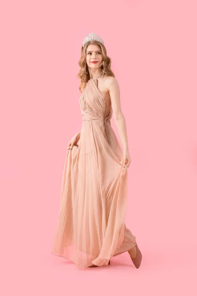 Teenage girl in tiara and prom dress on pink background