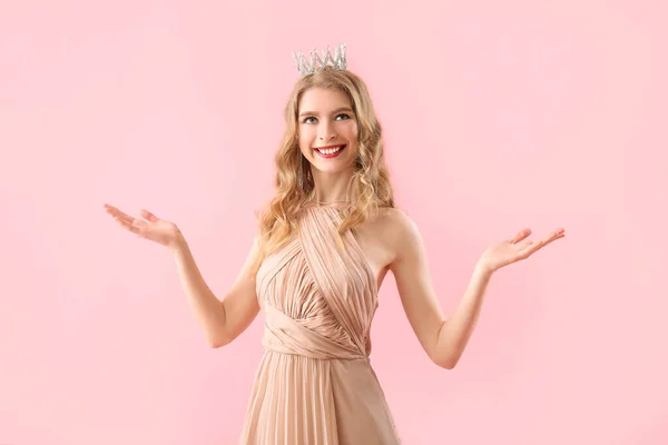 Teenage girl in crown and prom dress on pink background