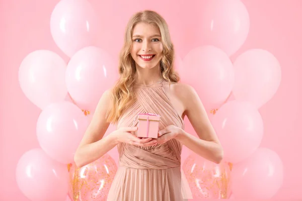 stock image Teenage girl in prom dress with gift and balloons on pink background