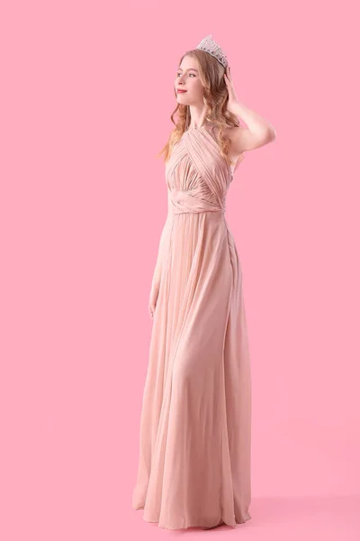 Teenage girl in tiara and prom dress on pink background