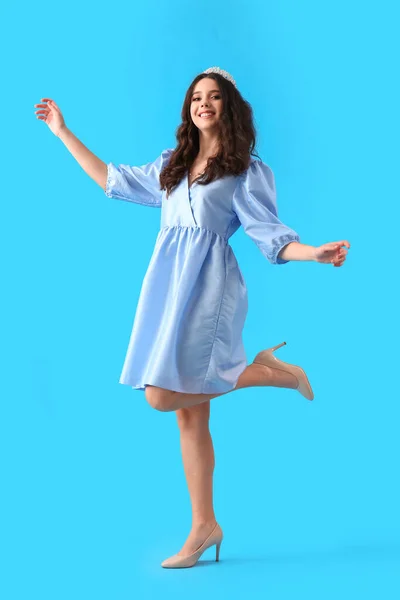 Teenage girl in tiara and prom dress dancing on blue background
