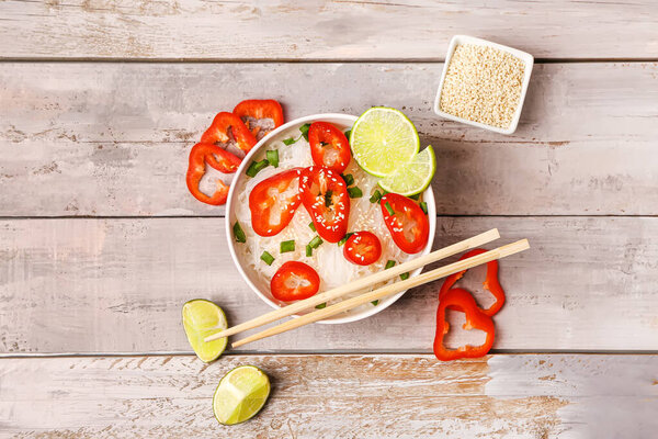 Bowl of tasty rice noodles with bell pepper, lime and sesame seeds on light wooden background