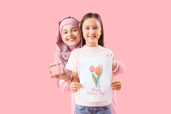 小さな女の子ともに挨拶カードとギフトのために彼女のイスラム教徒の母親上のピンクの背景 — ストック写真