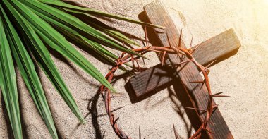 Crown of thorns with wooden cross and palm leaf on sand. Good Friday concept