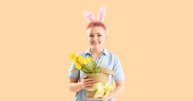 Young woman with Easter bunny ears and basket of tulips on beige background