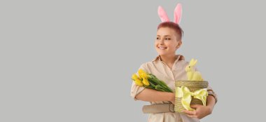 Young woman with basket, Easter rabbit and tulips on grey background with space for text
