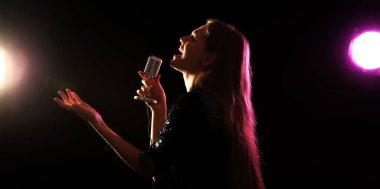 Emotional young woman singing in microphone on stage