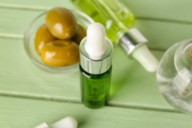 Bottle of olive essential oil on color wooden table, closeup