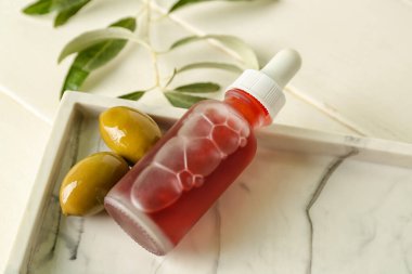 Bottle of olive essential oil on light wooden table, closeup