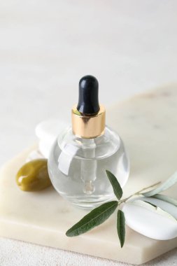 Board with bottle of olive essential oil on light background, closeup