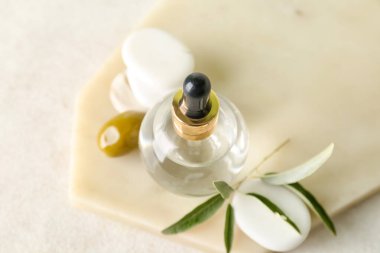 Board with bottle of olive essential oil on light background, closeup