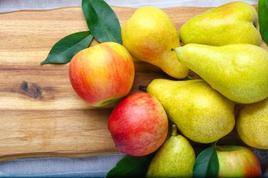 Wooden board with ripe pears and apples on table, closeup