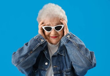 Senior woman in sunglasses on blue background, closeup