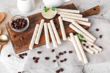 Board with delicious wafer rolls, coffee beans and condensed milk on white grunge background