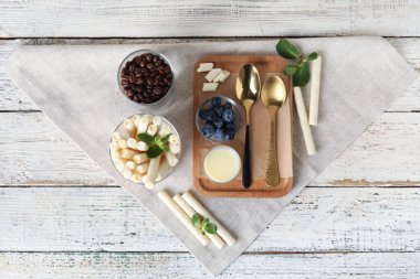 Glass of delicious wafer rolls and board with condensed milk on white wooden background