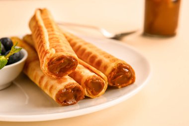 Plate of delicious wafer rolls with boiled condensed milk and blueberries on beige background