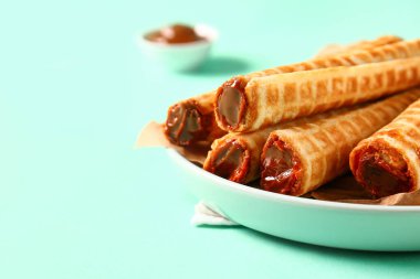 Plate of delicious wafer rolls with boiled condensed milk on turquoise background, closeup