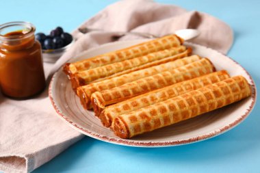 Plate of delicious wafer rolls with boiled condensed milk on blue background, closeup