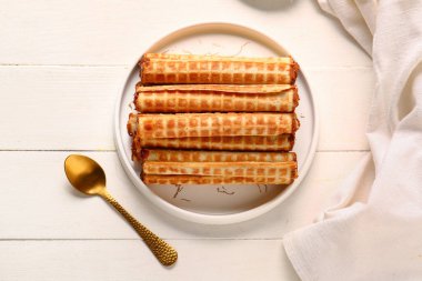 Plate of wafer rolls with boiled condensed milk and spoon on white wooden background