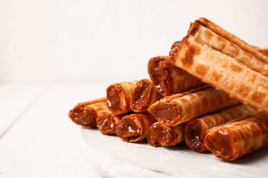 Stack of delicious wafer rolls with boiled condensed milk on white wooden table