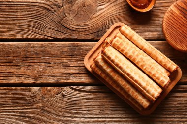 Board of wafer rolls with boiled condensed milk on brown wooden background