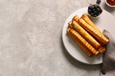 Plate of wafer rolls with boiled condensed milk and blueberries on grey grunge background