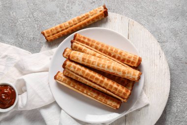 Plate of delicious wafer rolls with boiled condensed milk on grey grunge background