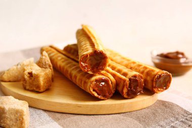 Delicious wafer rolls with boiled condensed milk on beige background