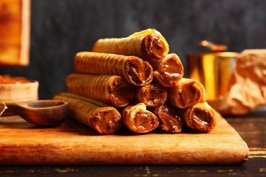 Stack of delicious wafer rolls with boiled condensed milk on black wooden table