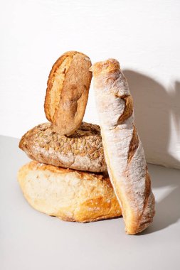 Loaves of different bread on table white wall