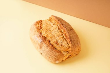 Fresh loaf of bread on yellow table against brown background