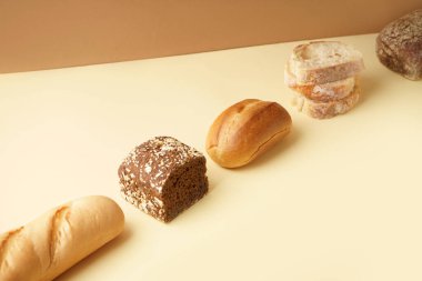 Loaves of different bread on beige table near brown wall