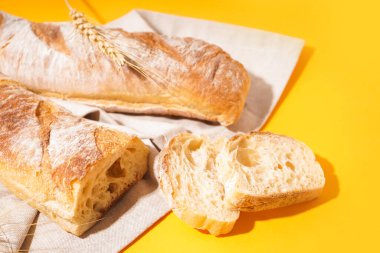 Fresh sliced baguette and wheat ears on yellow background