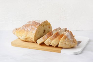 Board with sliced loaf of bread on white table