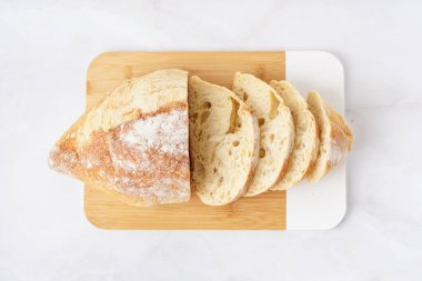 Board with sliced loaf of bread on white table