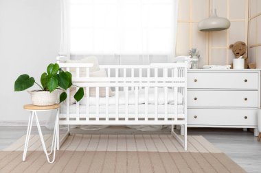 Interior of light children's bedroom with crib and commode