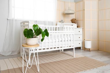 Interior of light children's bedroom with crib and commode