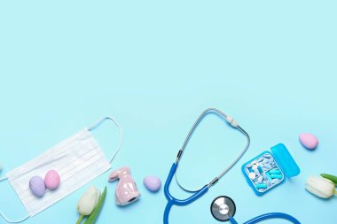 Stethoscope with medical mask, pills, tulips and Easter eggs on blue background. World Health Day
