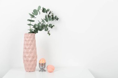 Vase with eucalyptus branches and Easter eggs on white background