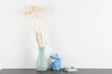 Vase with dried flowers, Easter eggs and rabbit on table near white wall
