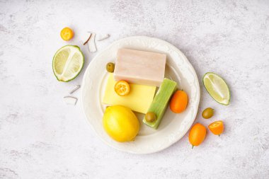 Plate with natural soap bars fruits and olives on light background