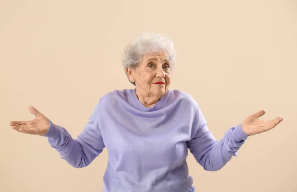 Confused senior woman in lilac sweater on beige background
