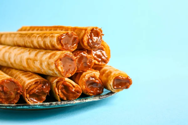 Plate of delicious wafer rolls with boiled condensed milk on blue background