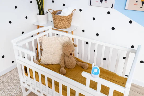 Crib with toy bear and baby monitor in children\'s bedroom