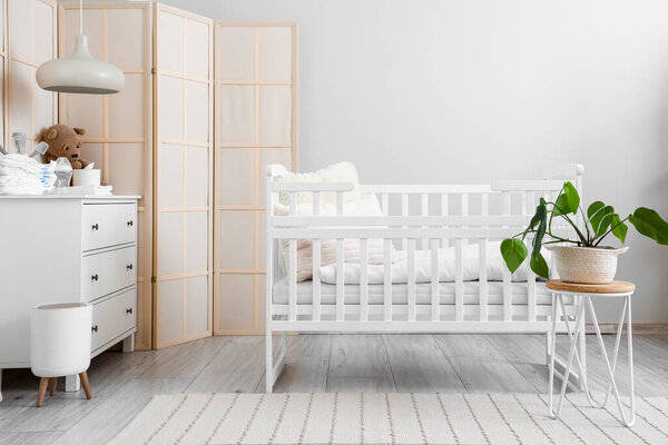Interior of light children's bedroom with crib and commode